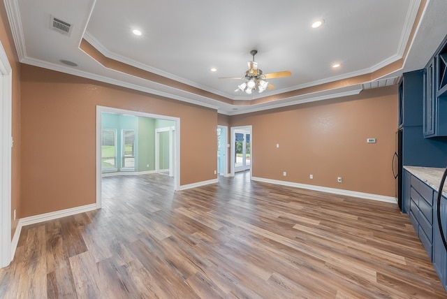 unfurnished living room featuring ceiling fan, light wood-type flooring, crown molding, and a tray ceiling