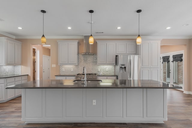 kitchen with decorative light fixtures, wall chimney range hood, stainless steel refrigerator with ice dispenser, and a large island with sink