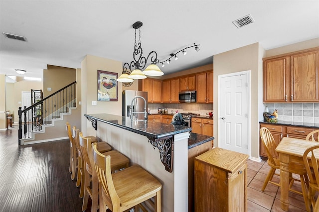 kitchen with a breakfast bar, hardwood / wood-style flooring, tasteful backsplash, decorative light fixtures, and stainless steel appliances