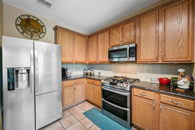 kitchen with dark stone countertops, light tile patterned floors, appliances with stainless steel finishes, and tasteful backsplash