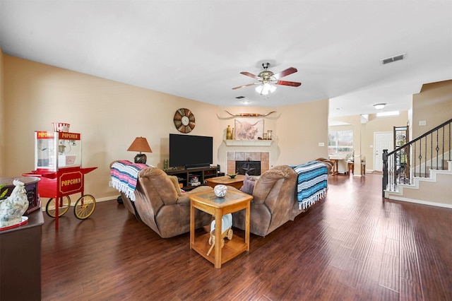 living room with a tiled fireplace, ceiling fan, and dark wood-type flooring