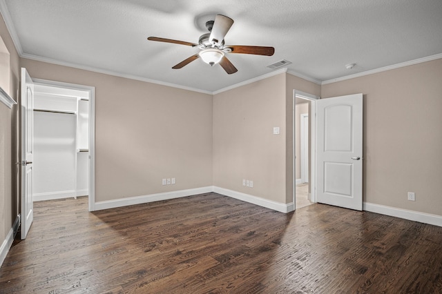 unfurnished bedroom featuring a walk in closet, crown molding, ceiling fan, dark hardwood / wood-style floors, and a textured ceiling