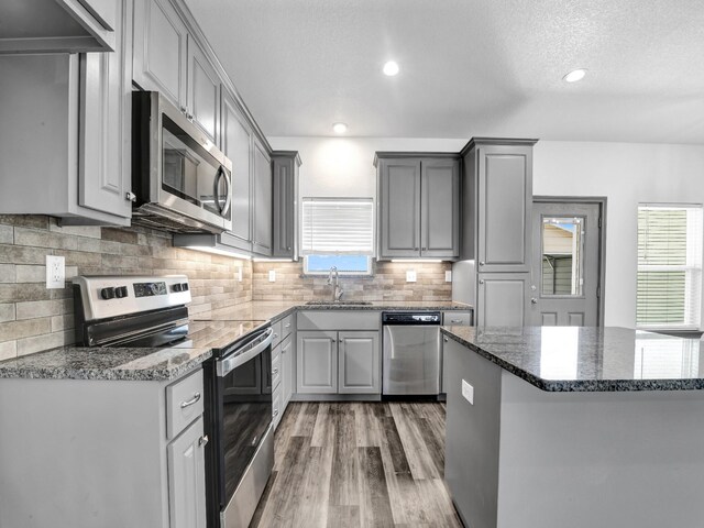 kitchen featuring stainless steel appliances, wood-type flooring, backsplash, gray cabinetry, and sink