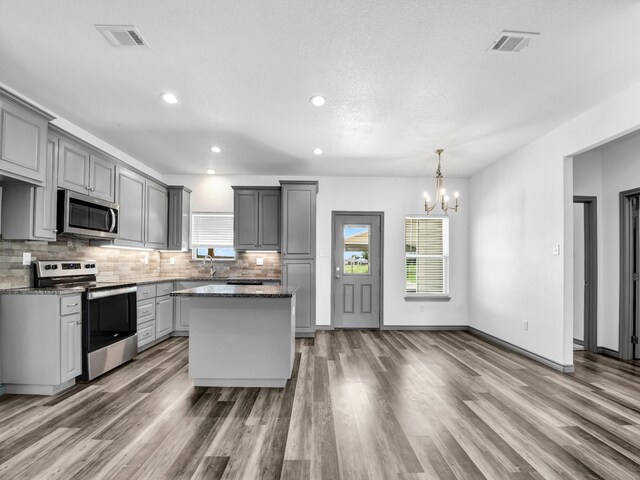 kitchen with hanging light fixtures, stainless steel appliances, gray cabinets, hardwood / wood-style flooring, and tasteful backsplash