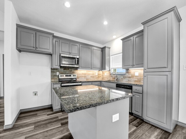 kitchen featuring dark stone counters, stainless steel appliances, gray cabinetry, a center island, and dark wood-type flooring