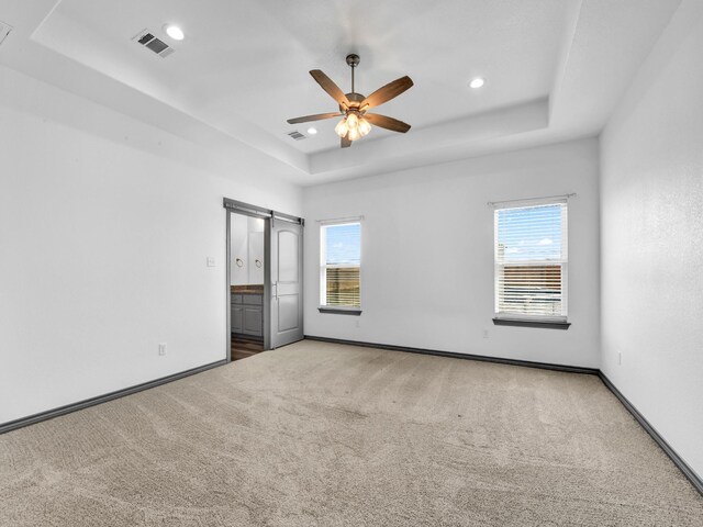 carpeted spare room with ceiling fan, plenty of natural light, and a tray ceiling