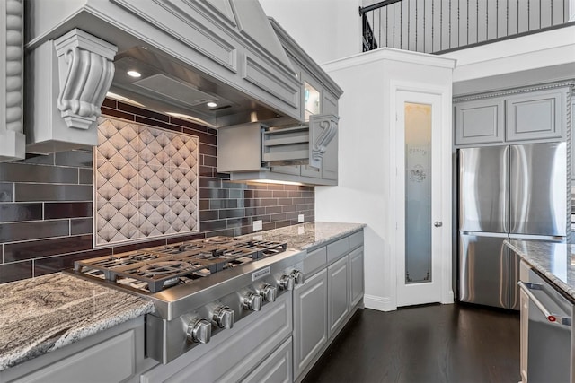 kitchen featuring decorative backsplash, gray cabinets, light stone counters, appliances with stainless steel finishes, and dark hardwood / wood-style flooring