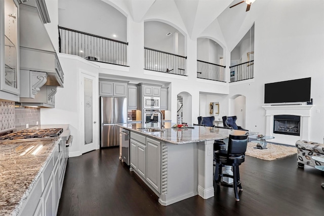 kitchen with a center island with sink, sink, gray cabinets, a towering ceiling, and stainless steel appliances