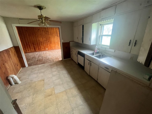 kitchen featuring dishwasher, white cabinetry, wooden walls, and sink