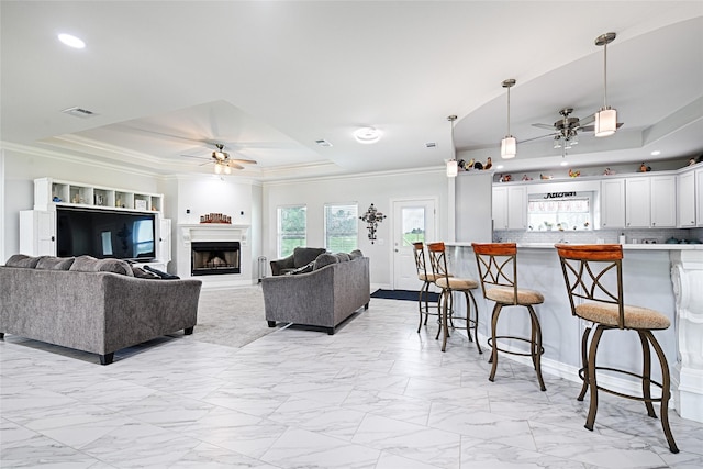 living room featuring a raised ceiling, ceiling fan, and ornamental molding