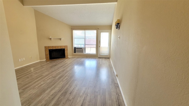 unfurnished living room with hardwood / wood-style flooring, cooling unit, a tile fireplace, and a textured ceiling