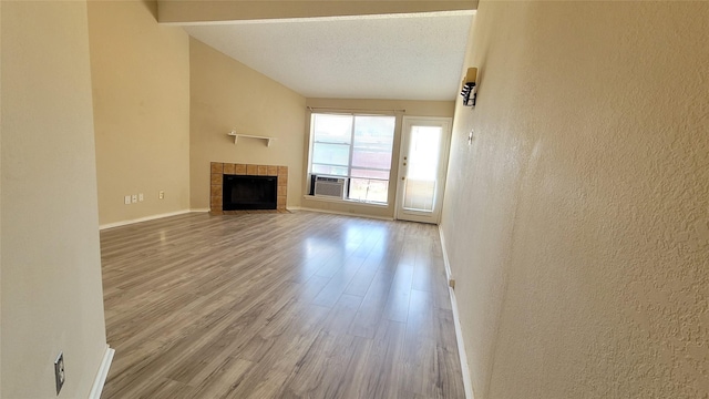 unfurnished living room with cooling unit, hardwood / wood-style flooring, a tile fireplace, and a textured ceiling