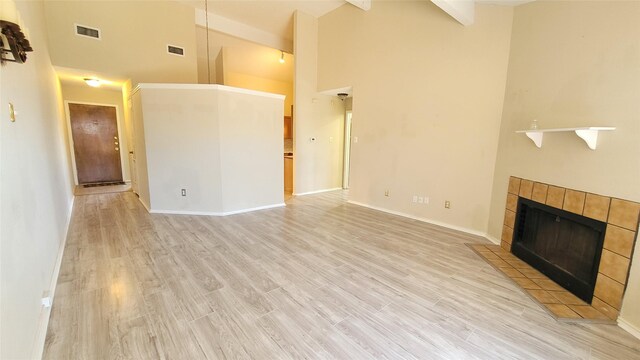 unfurnished living room with high vaulted ceiling, a tiled fireplace, and light wood-type flooring