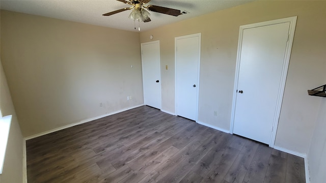 unfurnished bedroom with ceiling fan, multiple closets, and dark wood-type flooring