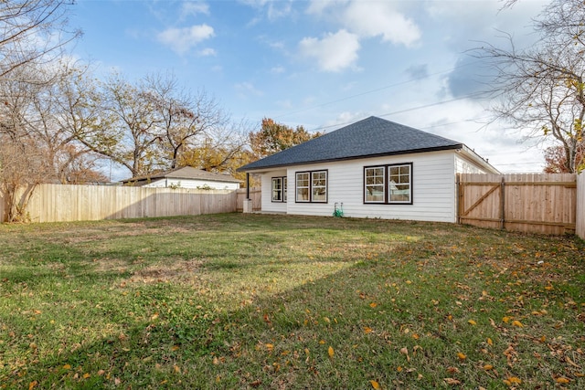 rear view of house with a lawn, a fenced backyard, and roof with shingles