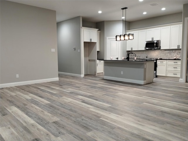 kitchen featuring white cabinetry, hanging light fixtures, light hardwood / wood-style flooring, appliances with stainless steel finishes, and an island with sink