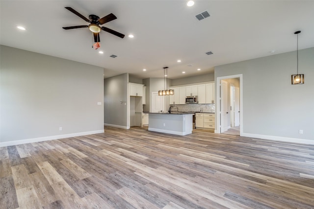 kitchen featuring white cabinetry, light hardwood / wood-style flooring, ceiling fan, a kitchen island with sink, and decorative backsplash