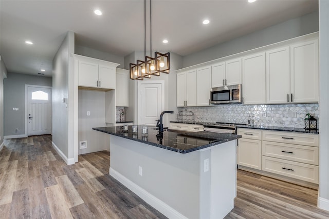 kitchen featuring an island with sink, white cabinetry, dark stone counters, hanging light fixtures, and light hardwood / wood-style floors