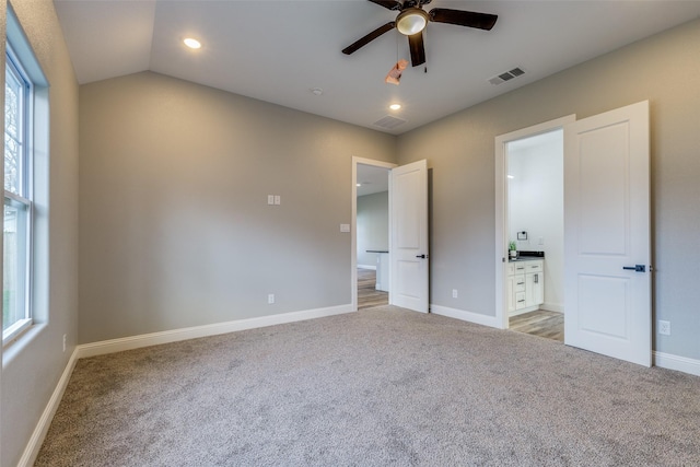 unfurnished bedroom with multiple windows, ceiling fan, vaulted ceiling, and ensuite bath