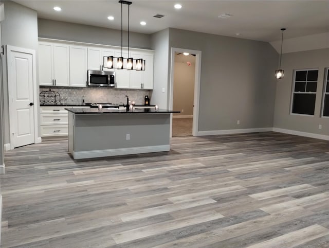 kitchen with white cabinetry, hanging light fixtures, light hardwood / wood-style floors, and an island with sink