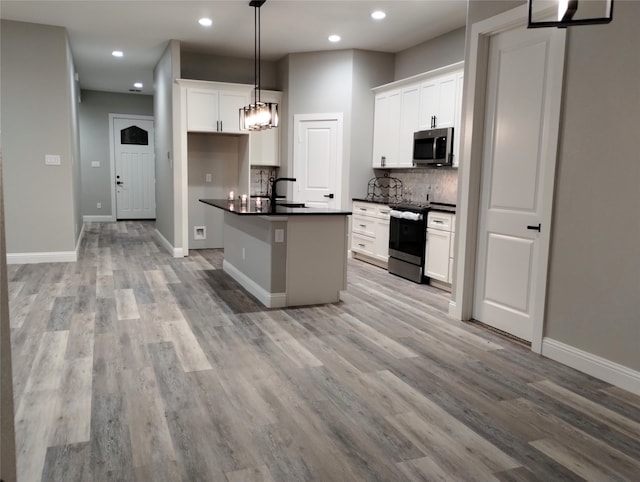 kitchen featuring appliances with stainless steel finishes, a kitchen island with sink, hanging light fixtures, backsplash, and white cabinets