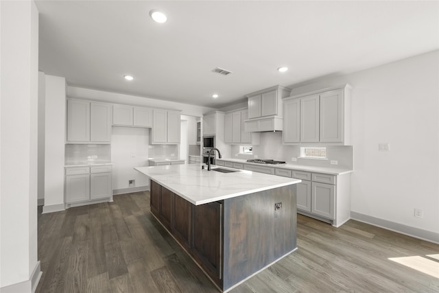 kitchen with backsplash, sink, light stone countertops, a kitchen island with sink, and wood-type flooring