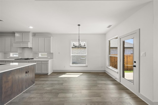 kitchen with dark hardwood / wood-style floors, hanging light fixtures, stainless steel gas stovetop, custom exhaust hood, and a notable chandelier