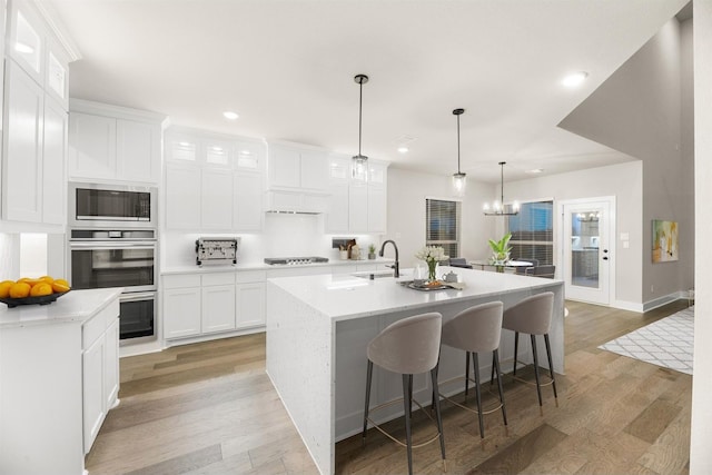 kitchen with a kitchen island with sink, white cabinets, light hardwood / wood-style floors, and appliances with stainless steel finishes