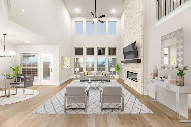 living room featuring light hardwood / wood-style floors, ceiling fan with notable chandelier, a towering ceiling, and a fireplace