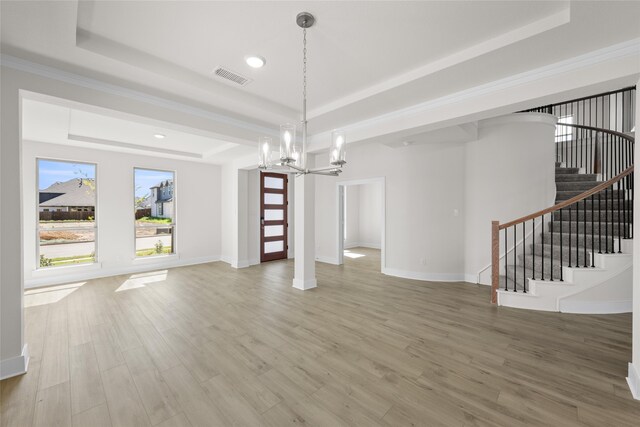 unfurnished living room with a raised ceiling, an inviting chandelier, ornamental molding, and hardwood / wood-style flooring