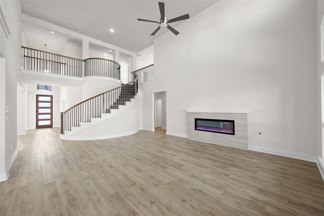 unfurnished living room with ceiling fan, light wood-type flooring, a fireplace, and a high ceiling