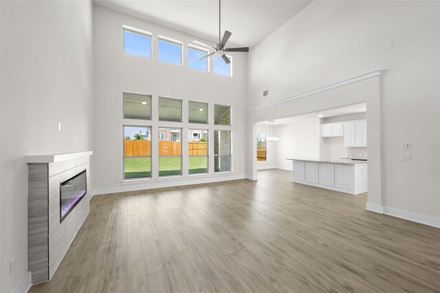 unfurnished living room featuring ceiling fan, light hardwood / wood-style floors, a towering ceiling, and a tiled fireplace