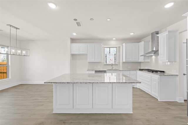 kitchen featuring white cabinets, a kitchen island, wall chimney range hood, and a healthy amount of sunlight