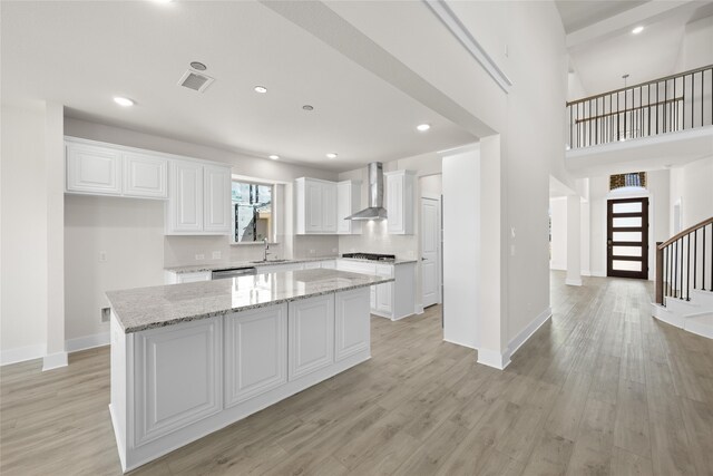 kitchen with a kitchen island, light stone countertops, wall chimney range hood, and white cabinetry