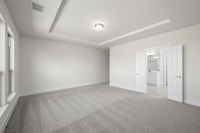 empty room with a raised ceiling and light carpet