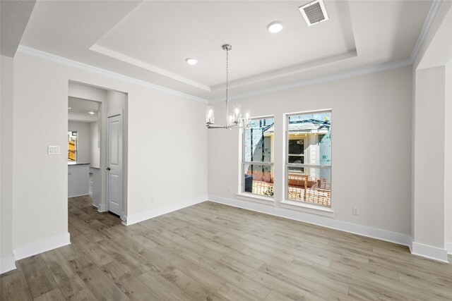 unfurnished dining area with a raised ceiling, crown molding, a chandelier, and light wood-type flooring