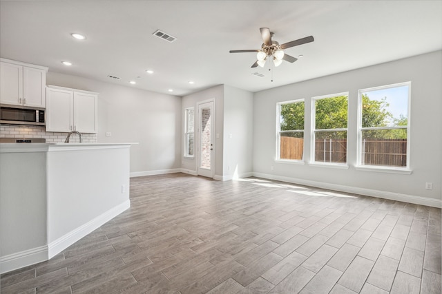 unfurnished living room with light wood-type flooring, ceiling fan, and sink