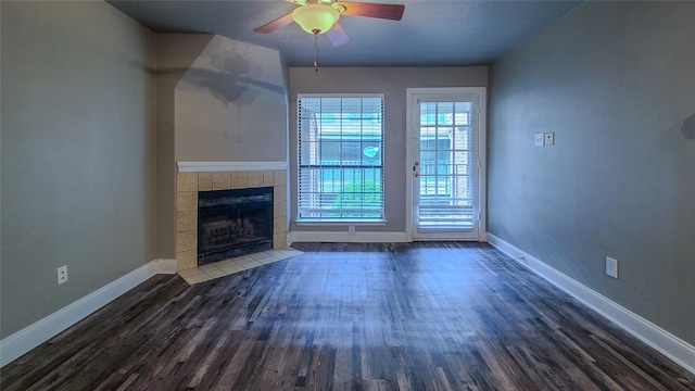 unfurnished living room with a tiled fireplace, ceiling fan, and dark hardwood / wood-style floors