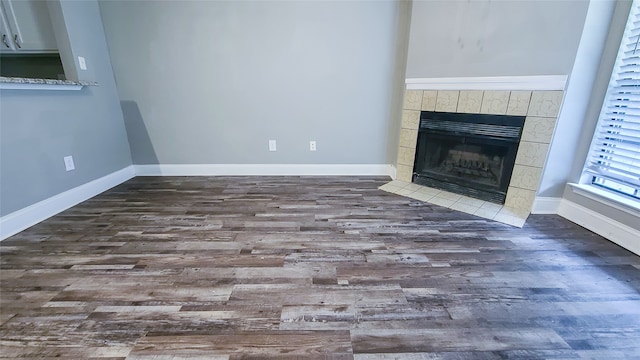 unfurnished living room featuring a tiled fireplace and dark hardwood / wood-style flooring