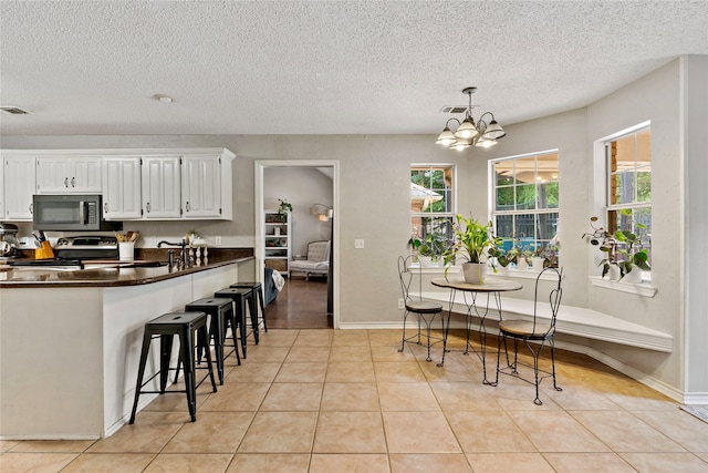 kitchen featuring a kitchen bar, white cabinets, electric stove, light tile floors, and pendant lighting