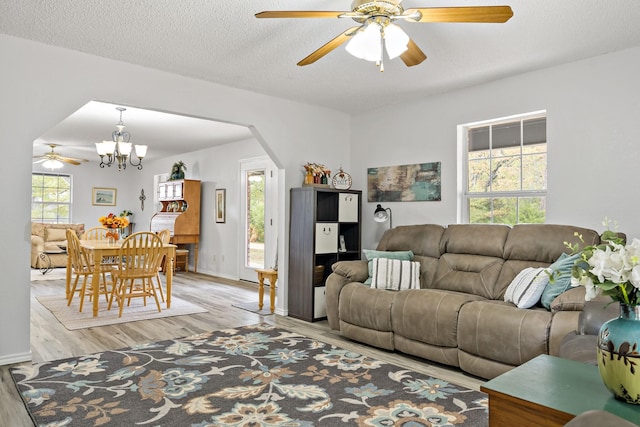 living room featuring ceiling fan with notable chandelier, a textured ceiling, and light wood-type flooring