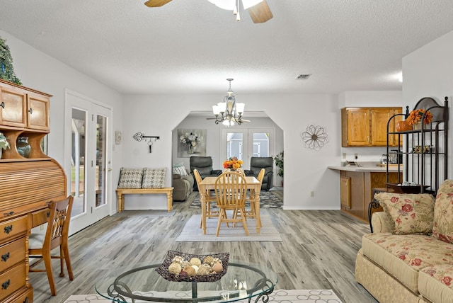 dining space featuring french doors, ceiling fan with notable chandelier, a textured ceiling, and light wood-type flooring