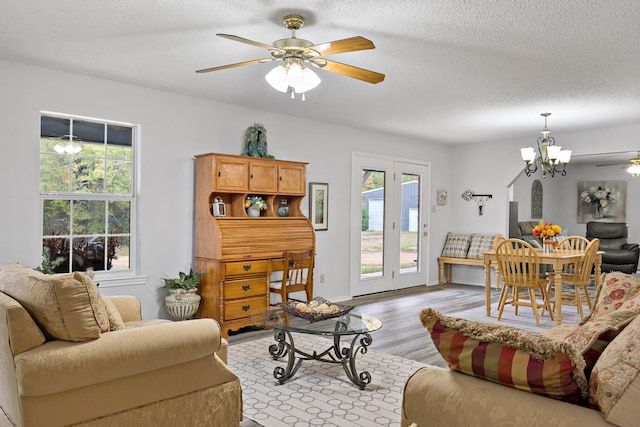 living room with ceiling fan with notable chandelier, light hardwood / wood-style floors, and a textured ceiling