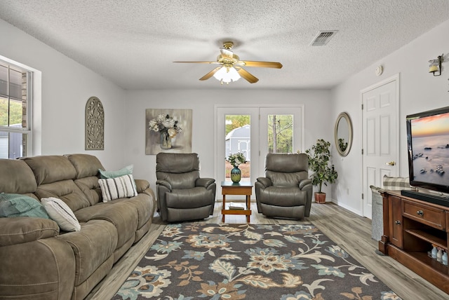 living room with ceiling fan, light hardwood / wood-style flooring, and a textured ceiling