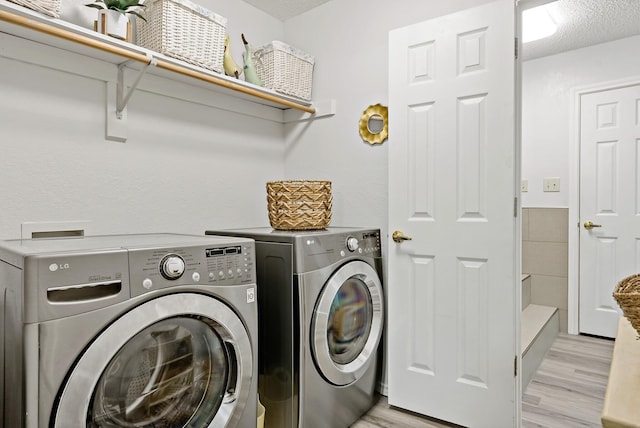 clothes washing area featuring washer and clothes dryer, a textured ceiling, and light wood-type flooring