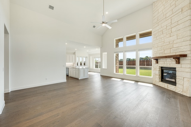 unfurnished living room with a stone fireplace, hardwood / wood-style floors, high vaulted ceiling, and ceiling fan