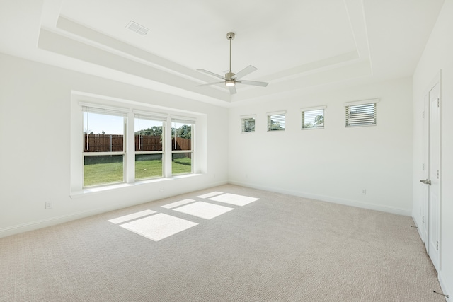 empty room with light carpet, a tray ceiling, and ceiling fan