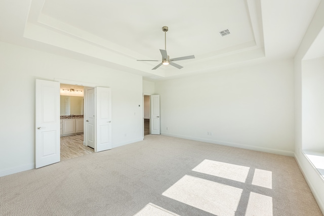 unfurnished bedroom featuring light colored carpet, a tray ceiling, and ceiling fan