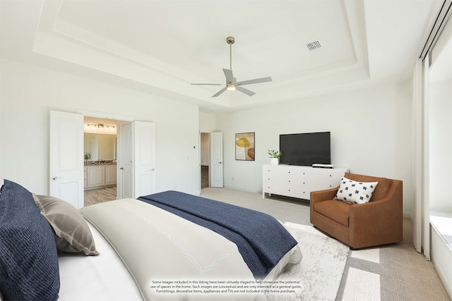 bedroom with light colored carpet, ceiling fan, a raised ceiling, and ensuite bath