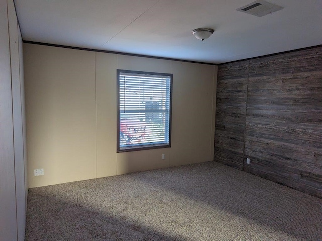 unfurnished room featuring visible vents, wood walls, and carpet